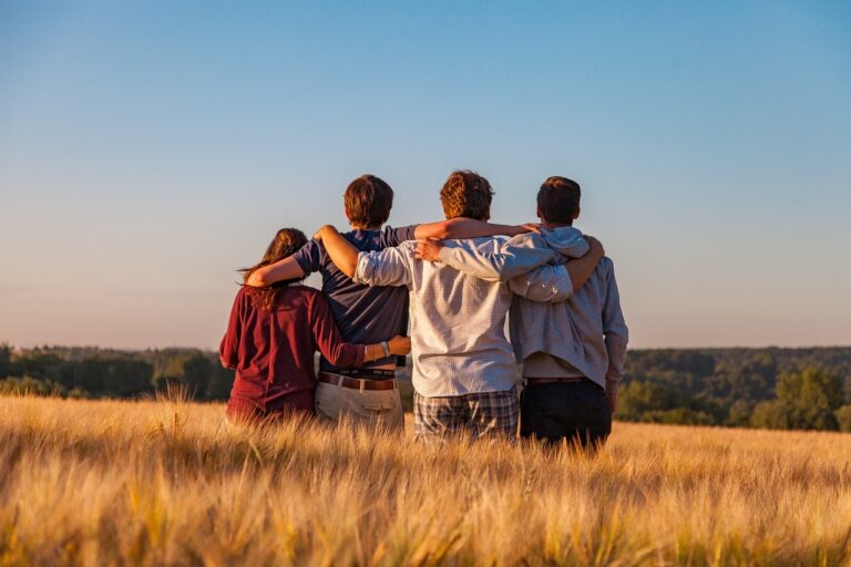 group of four teenagers with their backs to the camera sitting in a field discussing money saving ideas for teens